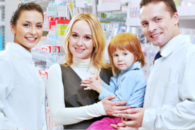 male and female pharmacist with the adult woman carrying her child smiling